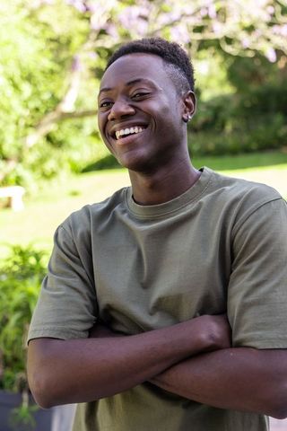 Smiling african man standing arms crossed in sunny garden wearing olive t-shirt casual