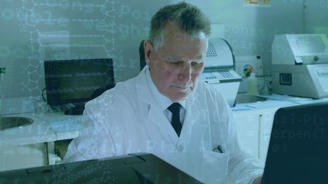 Senior male scientist in white lab coat focused on analyzing data on his computer in a laboratory environment. Ideal for content related to technology and scientific research, or depicting modern laboratory work practices.