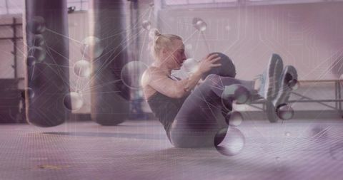 Mid-adult woman performing medicine ball russian twist in boxing gym with digital overlay