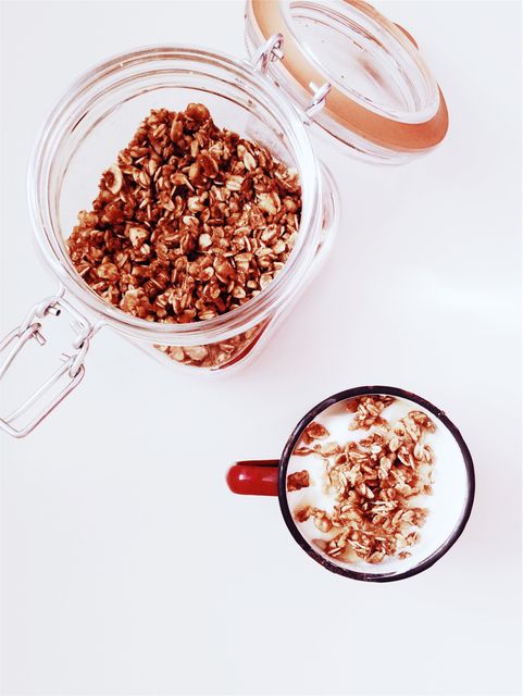 Granola spread in jar next to a mug of yogurt topped with granola. Ideal for illustrating healthy breakfast, nutritious snacks or meal preparation. Useful for diet websites, food blogs, recipe books, and wellness articles.