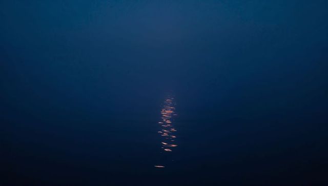Narrow vertical moonlight reflection stretching over calm deep blue water at night