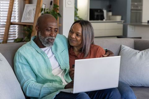 Mature couple managing household finances online on sofa with laptop and credit card