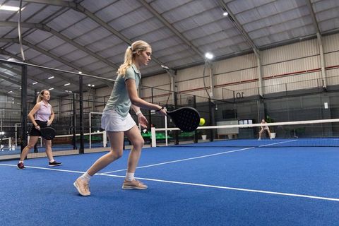 Women playing padel on indoor blue court hitting ball with black rackets, teamwork