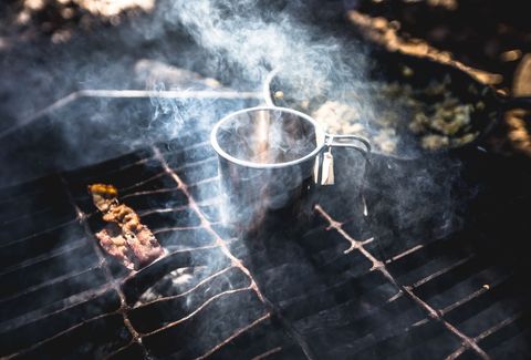 Campfire grill smoking with metal mug and sizzling bacon strip