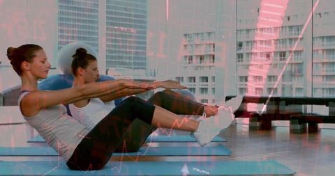 Two women performing v-sit core exercise on blue mats in fitness studio with data overlay