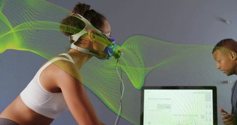 Woman undergoing vo2 max testing on ergometer with respiratory mask and technician monitoring