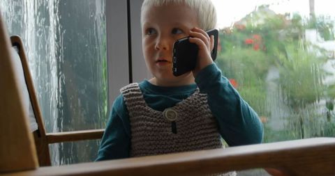 Cute toddler talking on phone by window