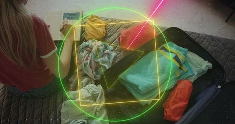 Packing suitcase and checking travel checklist on bed with colorful clothes and towels