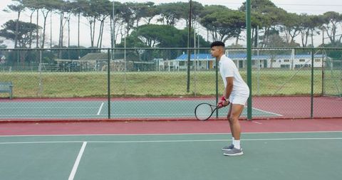 Adult male standing ready on outdoor tennis court holding racket wearing white outfit
