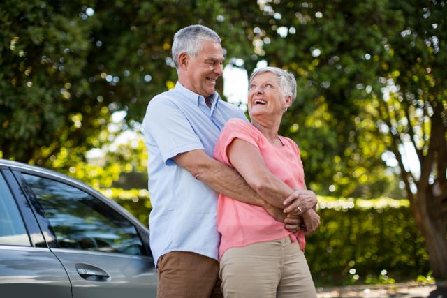Senior couple embracing and smiling outdoors by a car. Ideal for use in advertisements, retirement planning brochures, lifestyle blogs, and healthcare promotions focusing on senior well-being and happiness.