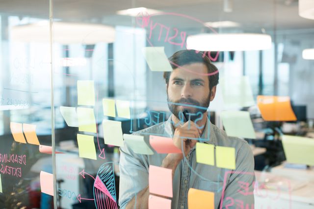 Thoughtful businessman looking at strategy written on glass at office