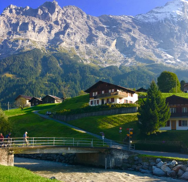 Beautiful Alpine village in Switzerland with green hills, traditional chalets, a flowing river, and majestic mountains. Perfect for travel brochures, nature-themed posters, and greeting cards highlighting Swiss scenery and outdoor adventures.