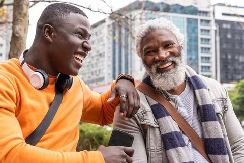African american friends laughing together on urban bench with smartphone and headphones