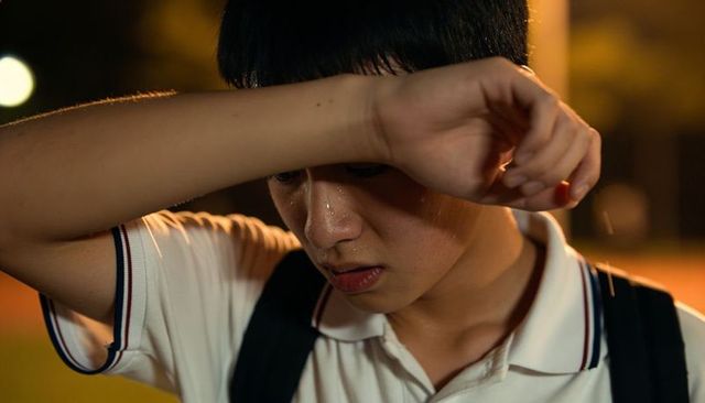Teen athlete wiping sweat and shielding eyes on night track after intense practice