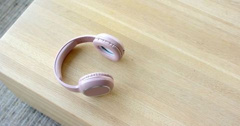 Pale pink wireless over-ear headphones resting on light wood table with minimalist pastel