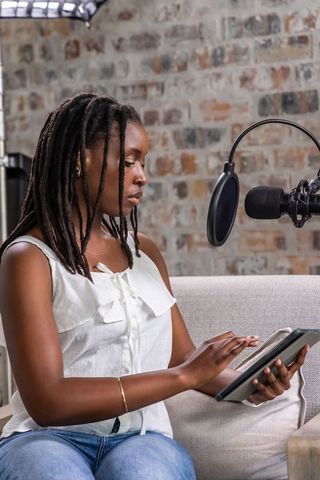 African american woman recording podcast on tablet in loft studio with microphone