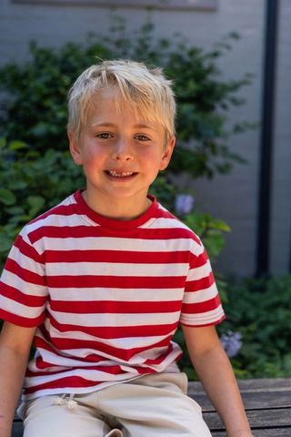 Smiling blond boy sitting on wooden bench red striped shirt outdoor garden portrait