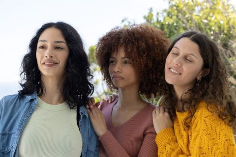 Diverse young women standing together by seaside, smiling and supporting each other