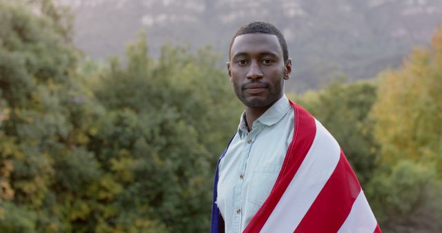 Portrait of african american man holding flag of usa in graden, copy space. Lifestyle, patriotism and celebration, unaltered.
