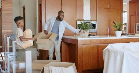 African American father and son unpacking boxes in sunlit modern kitchen, placing plants