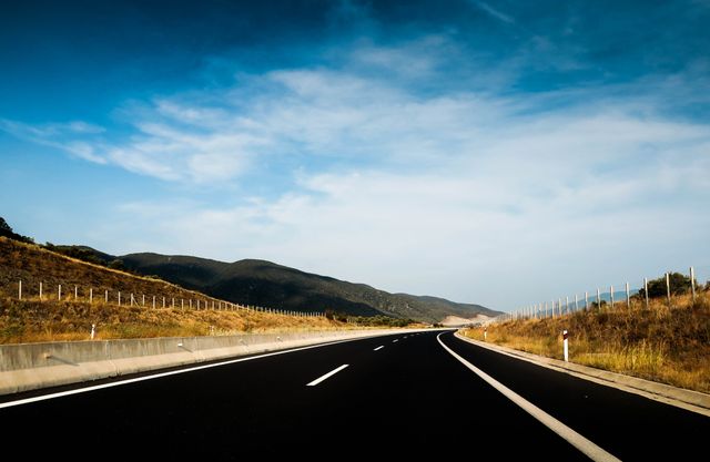 Curved highway passing through quiet countryside under blue sky. Ideal for illustrating concepts of travel, road trips, and adventure. Suitable for websites, blogs, advertisements related to transportation, logistics, and scenic routes.
