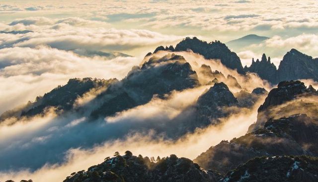 Sunrise fog rolling through jagged alpine ridge, sunlight bathing snow-dusted peaks
