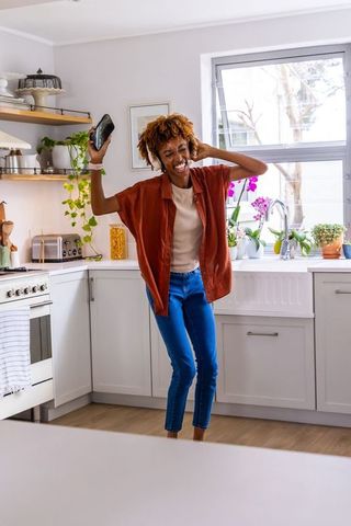 African american woman dancing in bright kitchen listening to music on headphones