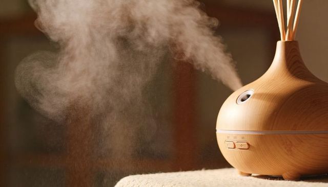 Wood-grain essential oil diffuser releasing warm mist on towel with reed sticks