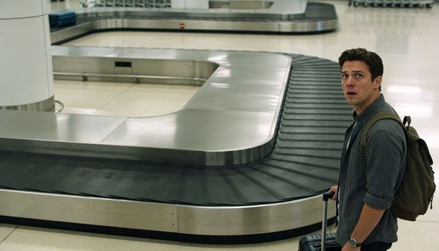 Solo traveler waiting at empty baggage carousel in modern airport terminal with suitcase
