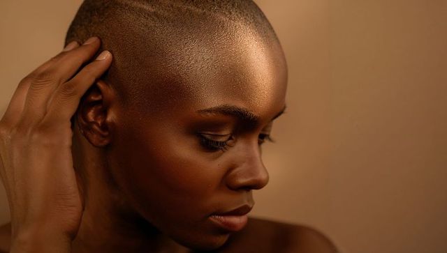 Closeup profile of woman touching shaved head with warm studio lighting, beauty portrait
