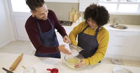 Couple baking together in bright home kitchen sifting flour and mixing batter