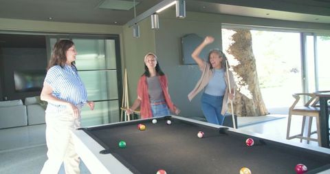 Three women playing pool in modern home celebrating casual billiards night