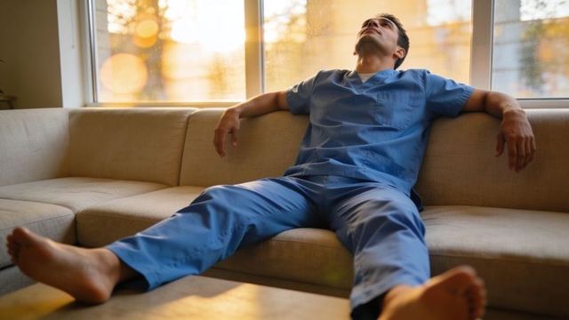 Exhausted healthcare worker reclining on sofa after long hospital shift at sunset