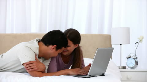 Happy Couple Relaxing with Laptop on Cozy Bed