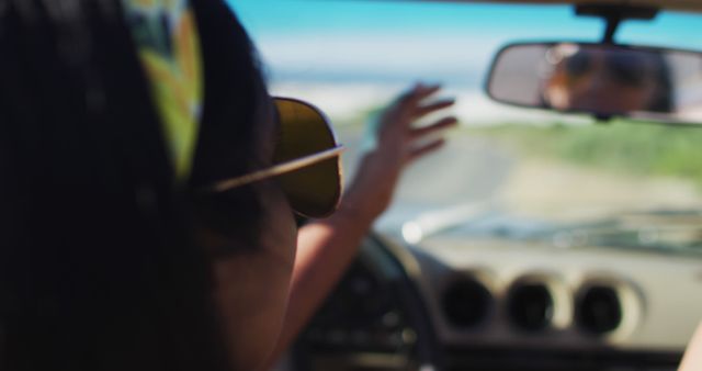 African american woman adjusting rear view mirror while sitting in the convertible car on road. road trip travel and adventure concept