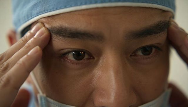 Surgeon pressing temples and adjusting surgical cap while preparing for surgery