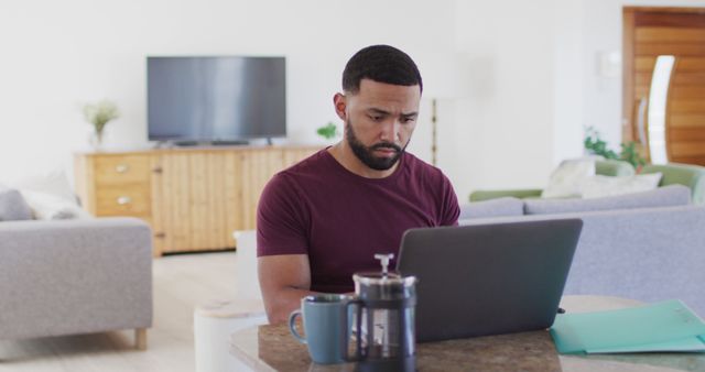 Man working on a laptop at home in a modern, well-lit living room. This image can be used for articles about remote work, productivity, home office setups, and modern living lifestyles.