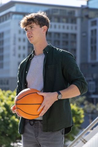 Teen holding basketball on rooftop terrace with city skyline, casual shirt and wristwatch