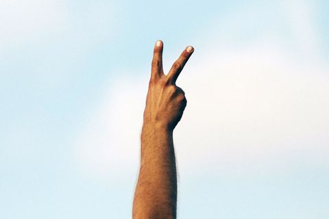 Hand Posing Peace Sign Against Blue Sky Background