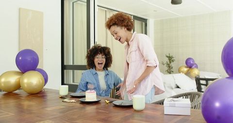 Two African American Women Celebrating Birthday at Dining Table with Cake and Balloons
