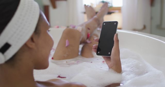 Biracial woman taking a bath and using smartphone. domestic life, spending quality free time relaxing at home.