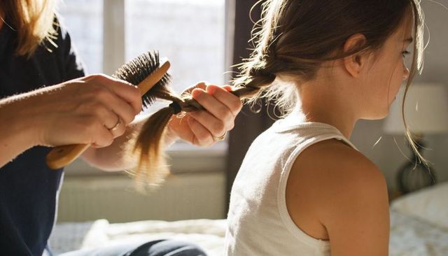 Braiding morning routine for school-age girl on bed in warm backlight