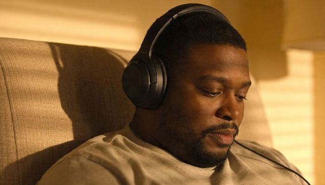 Sunlit man listening with headphones relaxing in cozy living room chair