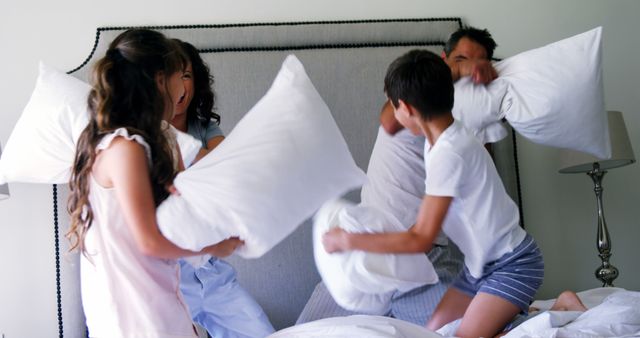 Parents and children engaging in a joyful pillow fight on bed in bedroom. Can be used for family, bonding, playful moments, morning routines, and advertisements showcasing a happy family life.