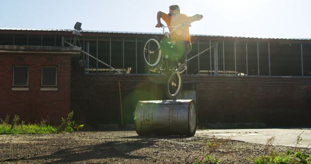 Man performing a BMX trick outside on industrial terrain with an afternoon sun flare. Perfect for use in sports advertisement, urban lifestyle blogs, extreme sports promotion, or adventure-themed projects.