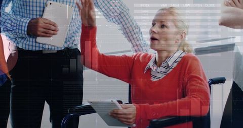 Senior woman in wheelchair presenting business data on tablet during collaborative meeting