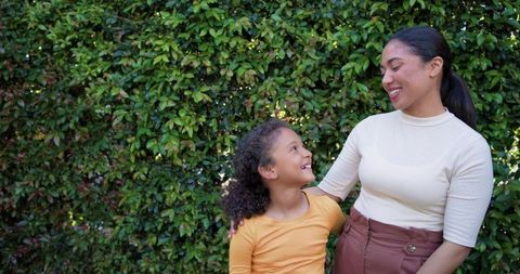 Mother and daughter sharing warm moment in sunlit garden, smiling and embracing