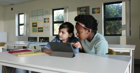 African American and Asian girls collaborating on tablet in classroom, teamwork and learning