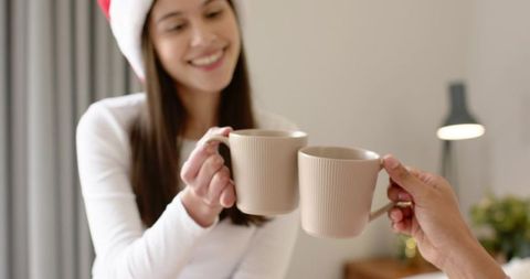 Smiling woman clinking beige ribbed mugs with friend during cozy christmas morning toast