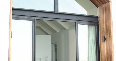 Contemporary black-framed sliding door with timber cladding, transom window and sheer curtain